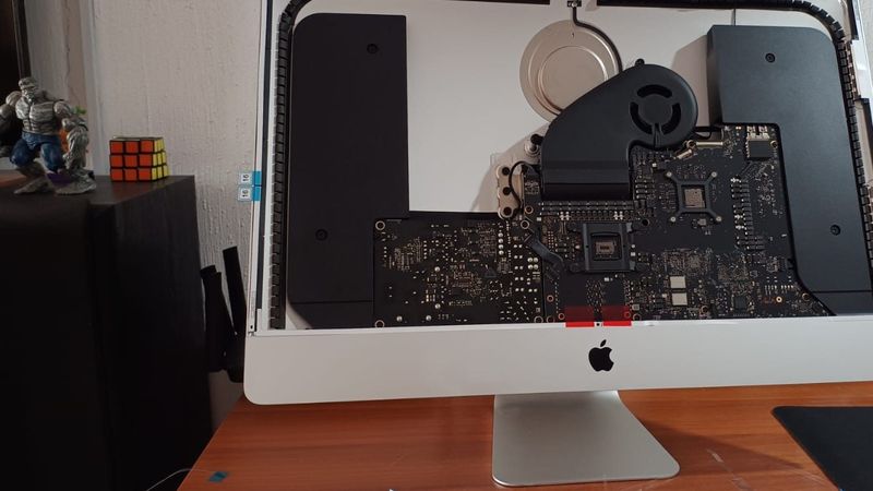 iMac abierta sin pantalla en el taller, con la placa lógica y el ventilador expuestos durante la reparación