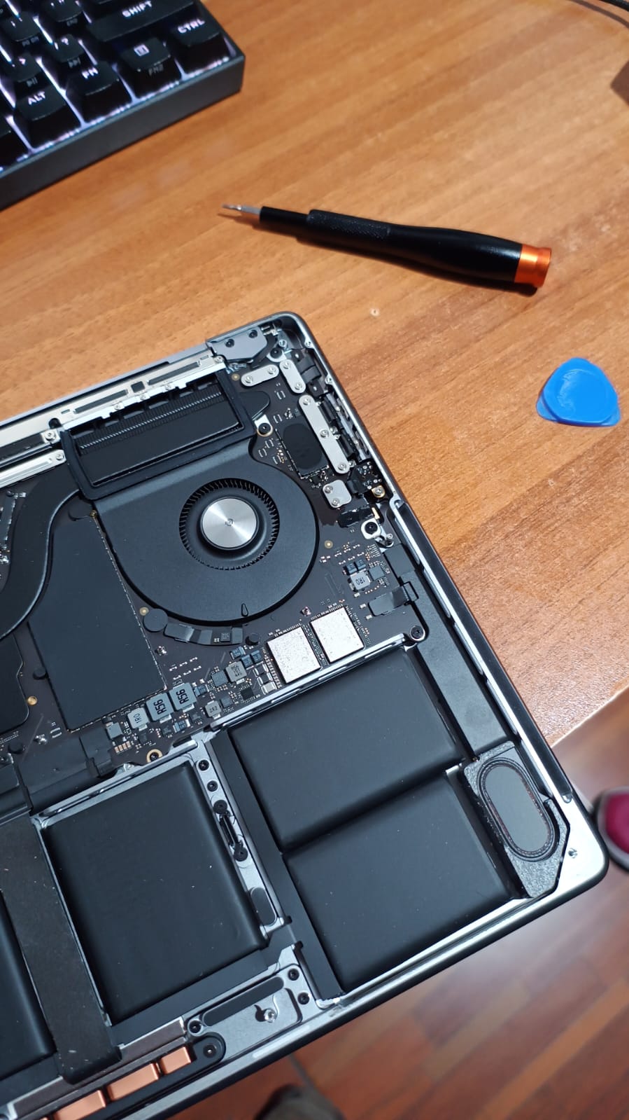 MacBook Pro abierta junto a un destornillador de precisión y una púa de apertura, lista para el cambio de batería